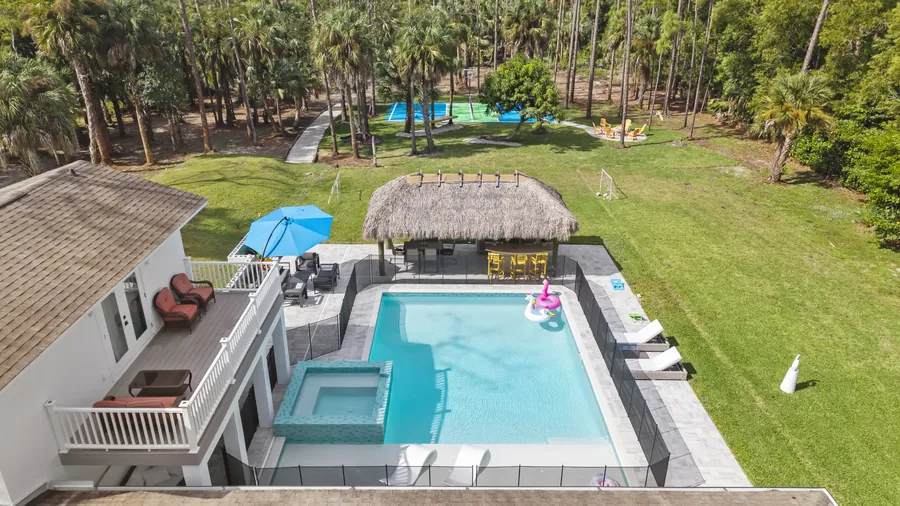 Aerial over pool and spa toward tiki hut, lawn, fire pit and pickleball court, The Naples Retreat, Naples FL