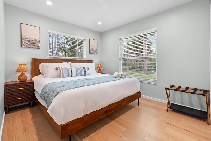 King bedroom with walnut bed, blue-gray throw and two windows to the trees, The Naples Retreat, Naples FL