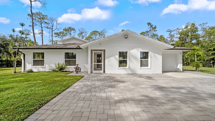 White ranch-style front of the home with paver driveway and green lawn, The Naples Retreat, Naples FL