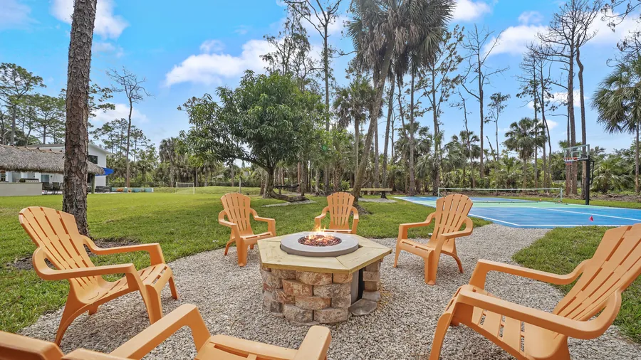 Fire pit ringed by Adirondack chairs on a gravel circle near the court, The Naples Retreat, Naples FL