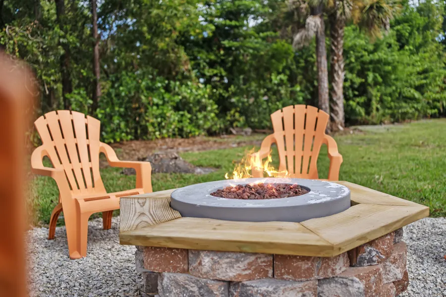 Lit gas fire pit with Adirondack chairs among the pines, The Naples Retreat, Naples FL
