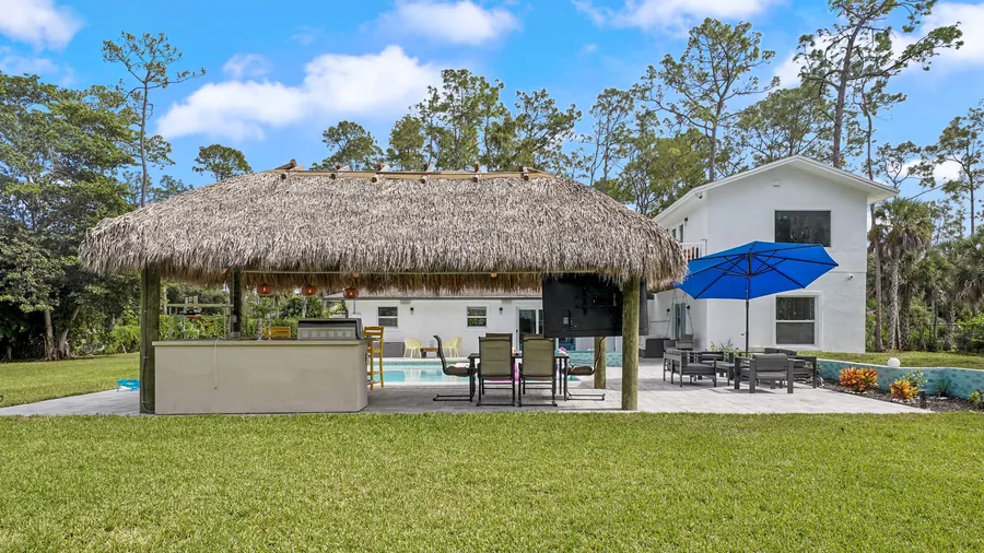 Thatched tiki cabana with bar and dining beside the pool, seen across the lawn, The Naples Retreat, Naples FL