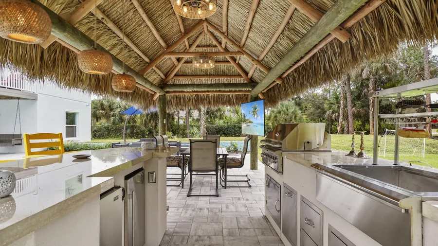 Tiki cabana outdoor kitchen with grill, bar seating and TV under thatched roof, The Naples Retreat, Naples FL